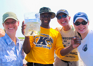 Photo of three students and teacher holding a plastic bag holding fish and underwater grasses.
