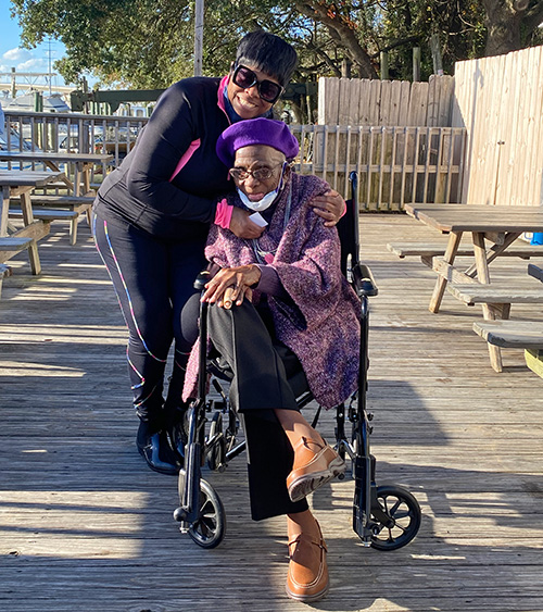 A woman leans over to hug an elderly woman in a wheelchair.