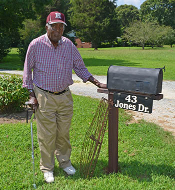 A man standing next to his mailbox in front of his house with oyster tongs nearby.