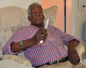 A man sits in his living room arm chair with a bunt needle used to craft and mend fishing nets.