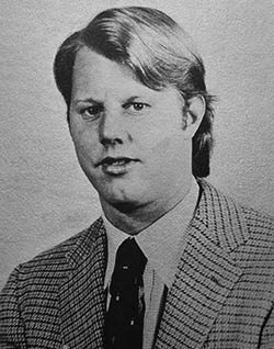 Old, black and white, headshot of a man wearing a tweed jacket.