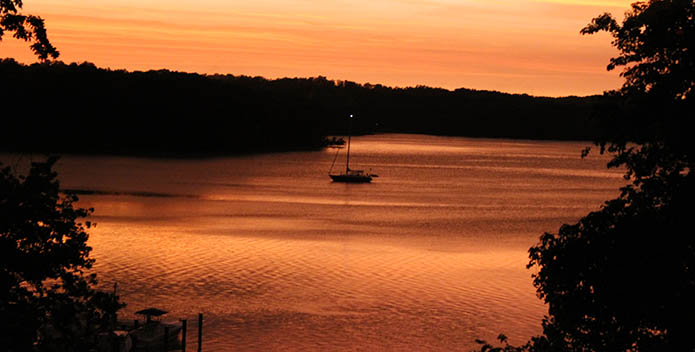 Photo of a sailboat on the river at sunset.