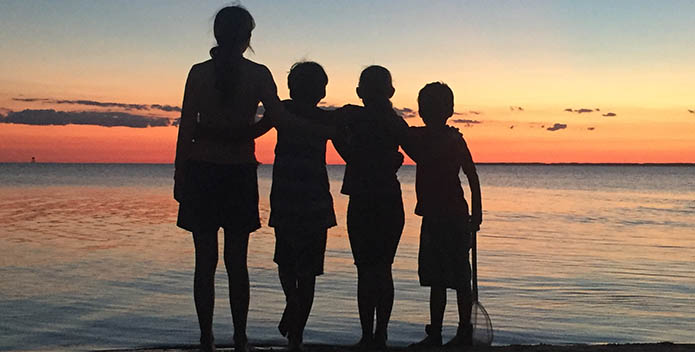 Silhouette of four children at the waters edge, backlit by a sunset.