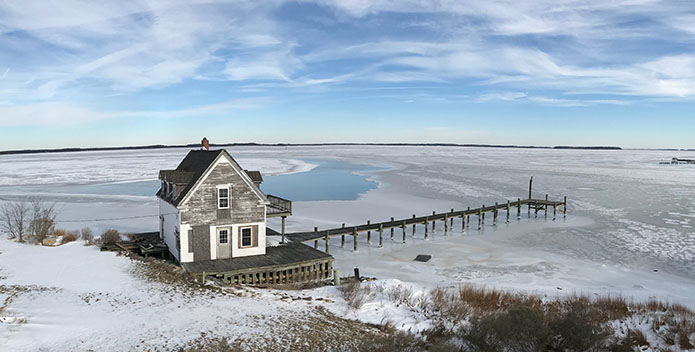 Photo looking down on the frozen Honga River with a lone white house in the foreground.