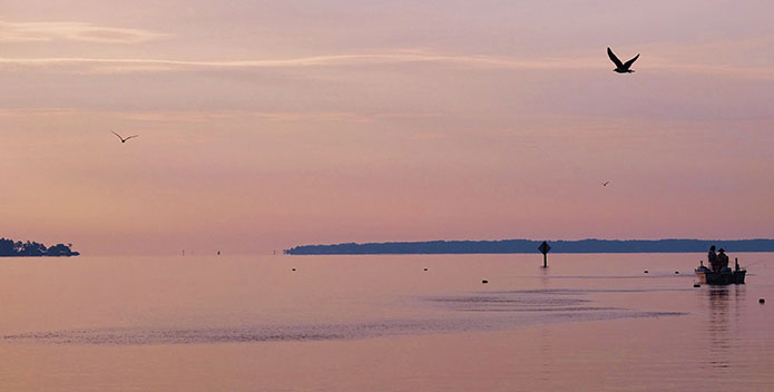 Sunset Palace Bar Reef. Bait fish create ripples on the water as silhouetted fishermen wait for a bigger catch.