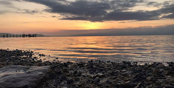 An orange sunrise lights up the sky above a rocky shore.