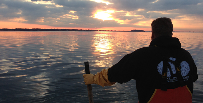 Photo of a waterman oystering as the sun rises over the Bay.