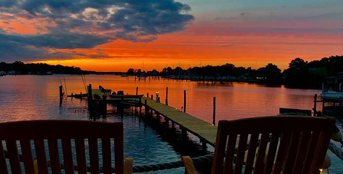 A fiery sun sets over Lake Ogleton with Adirondack chairs in the foreground