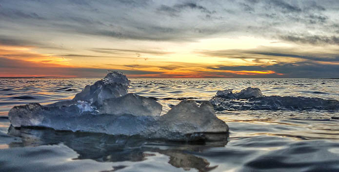 Photo of ice floating on water with the sun setting behind.