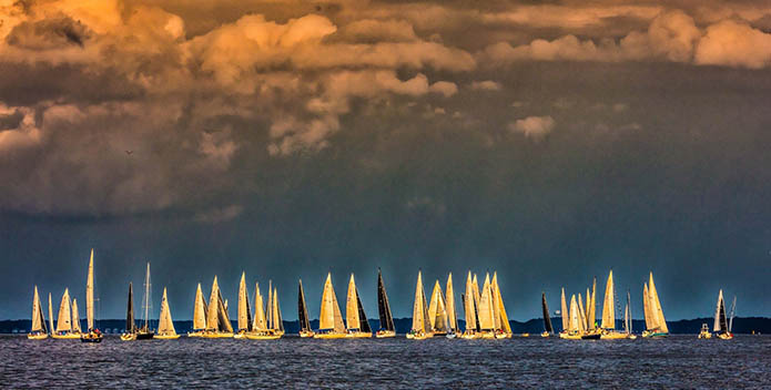 Photo of sailboats on the water against a backdrop of clouds lit by the setting sun.