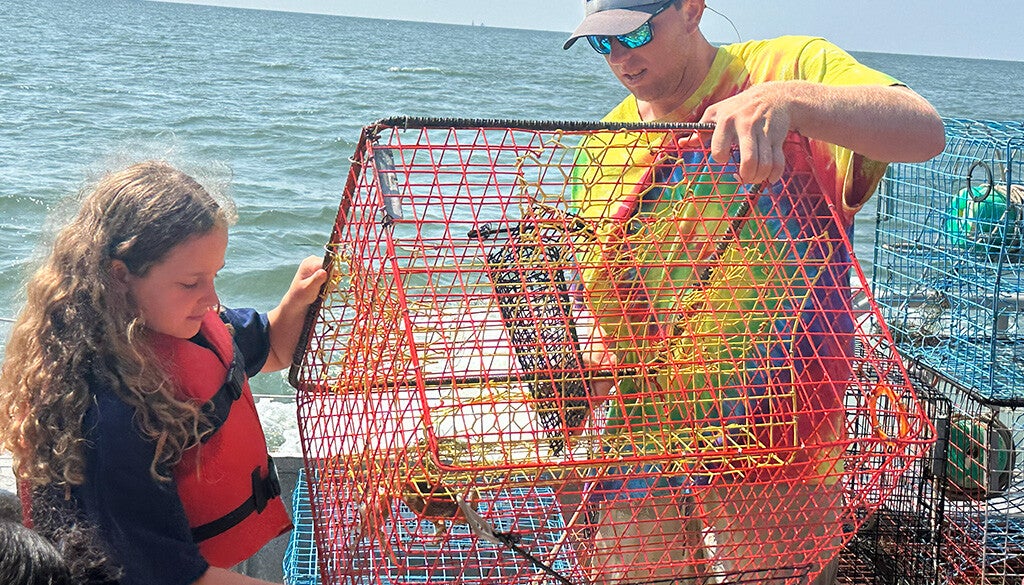 A man and a girl inspect a brightly colored crab pot on a sunny day on the Bay.