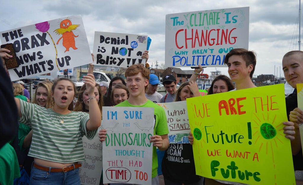 Youth climate activists hold handmade protest signs advocating for environmental justice and urgent climate action during a public demonstration.