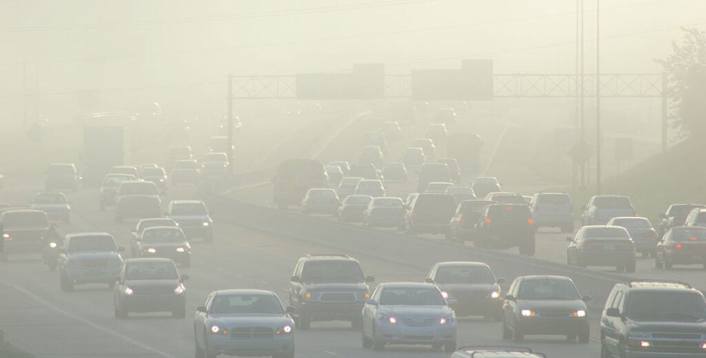 Heavy traffic on a highway shrouded in thick smog and air pollution with reduced visibility.