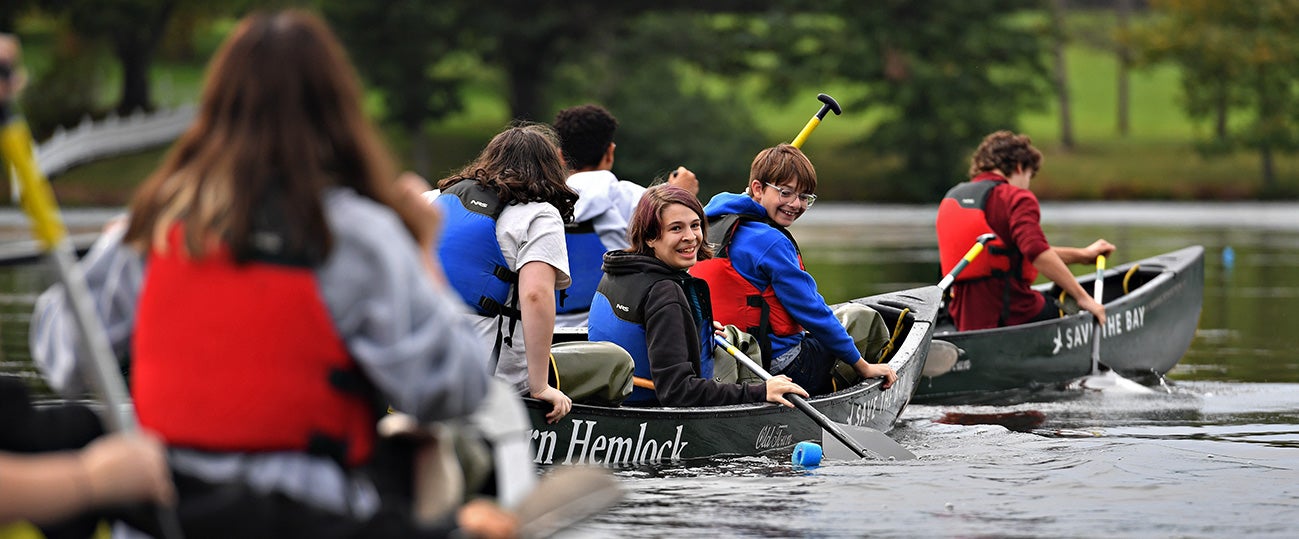 Students smile as they canoe on a river.