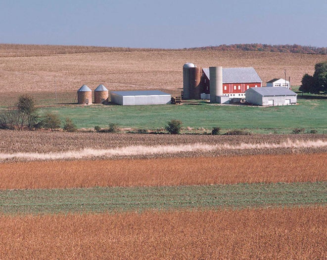A red barn with silos and outbuildings sits in the middle of several fields.