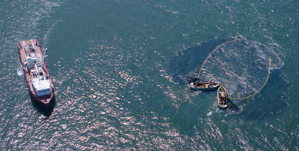 Two small boat circle a large school of menhaden with a net while a larger boat apporaches.
