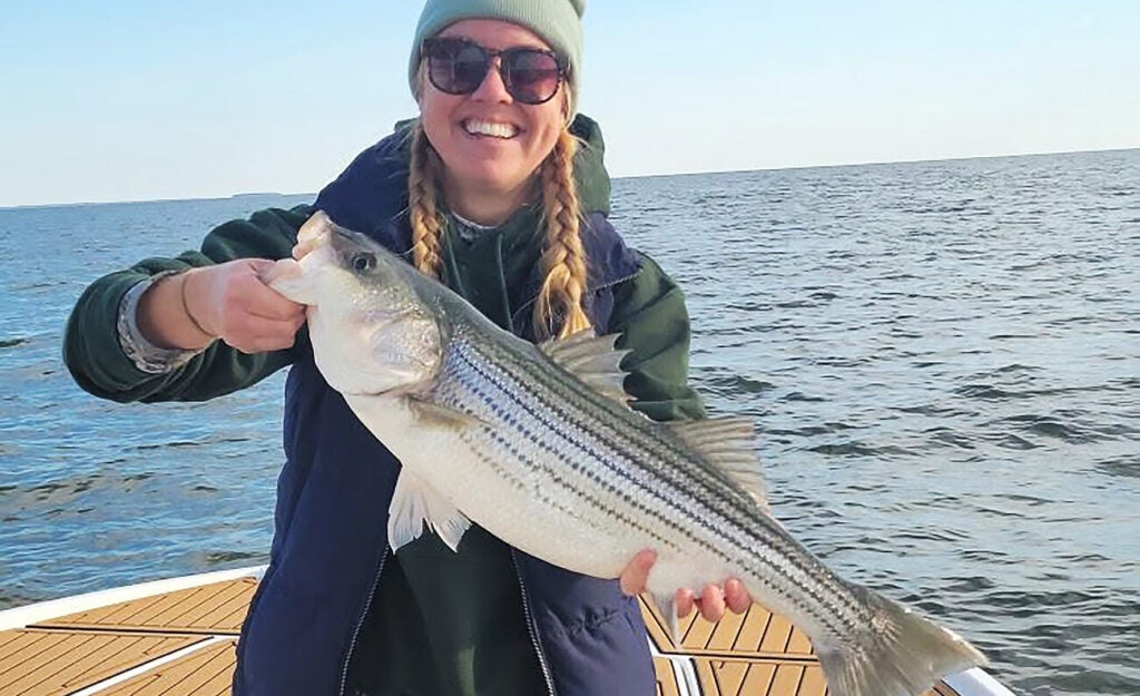 A smiling woman holds a freshly caught striped bass.
