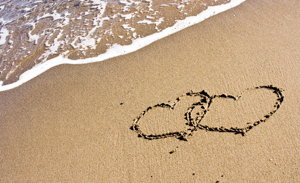 Two romantic hearts drawn in the sand next to a foamy wave.