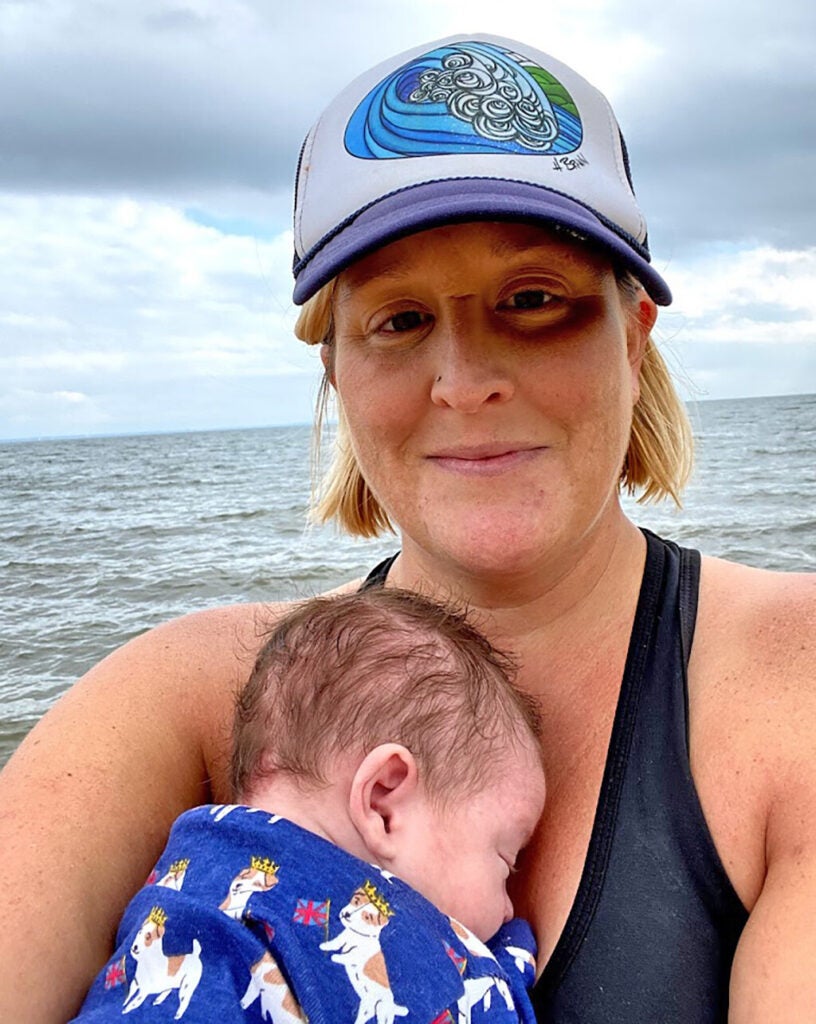 A smiling woman holds a little baby. The Bay is in the background.