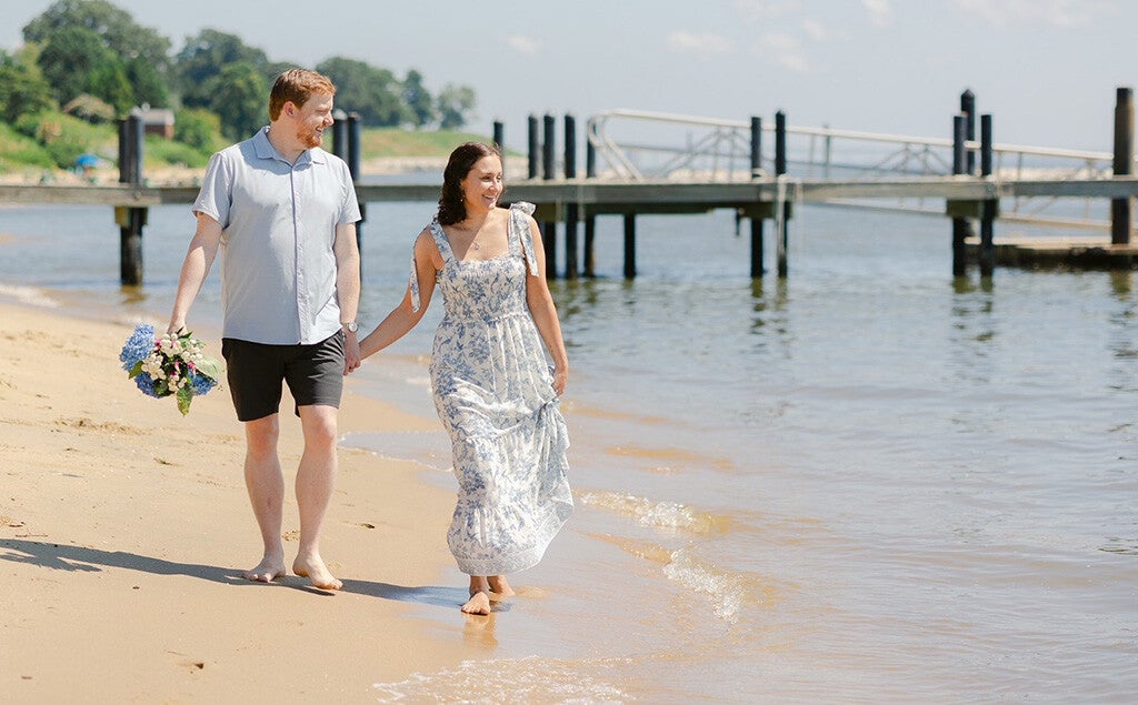 A man and woman holding hands walk along a beach.