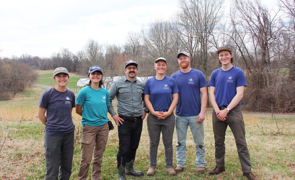 Six people stand in a field smiling at the camera.