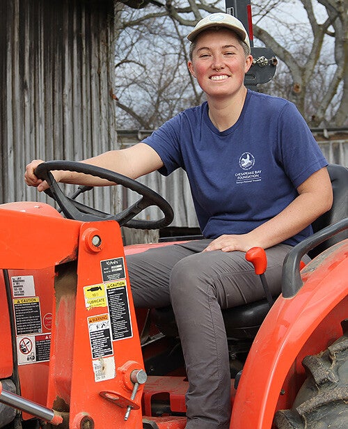Olivia Murphy, in a tan ball cap and blue CBF t-shirt, sits on an orange tractor.
