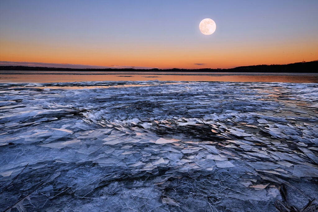 The moon rises over a river covered with a whirlpool of ice fragments.
