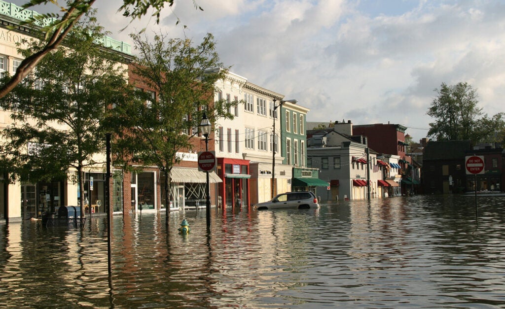 A flooded street, with water up to the top of a parked car's tires.