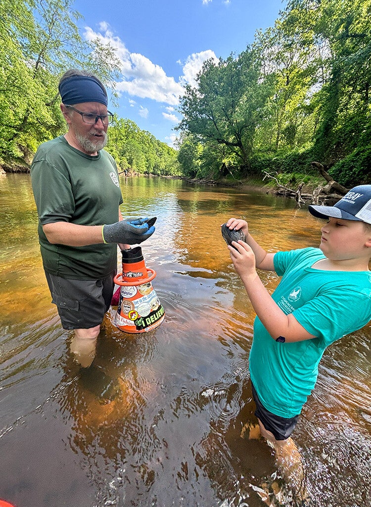A man and young boy stand in a stream and examine mussels they found.