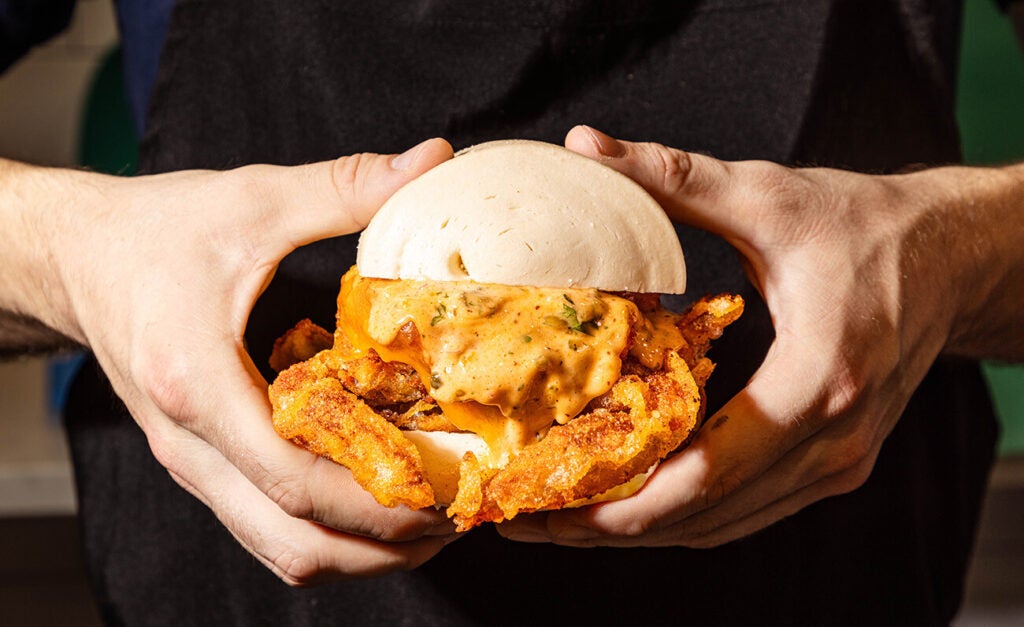 A close-up shows a person holding a crispy soft-shell crab sandwich inside a white bun.