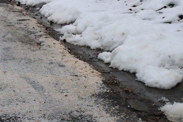 Road salt and sand mix with melting snow piles beside the pavement