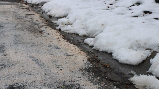 Road salt and sand mix with melting snow piles beside the pavement.