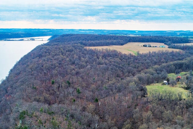 Aerial view of a forested peninsula extending into a reservoir with farmland and scattered buildings visible beyond.