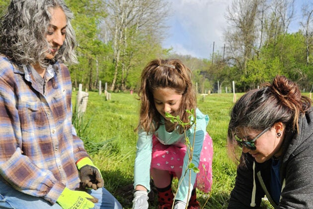 Two women and a young girl prepare to plant a tree.