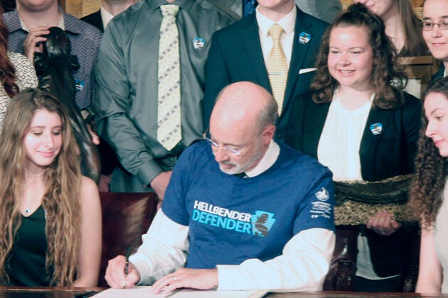 Former Governor Wolf wears a Hellbender Defender shirt and signs legislation surrounded by young advocates at a bill signing ceremony.