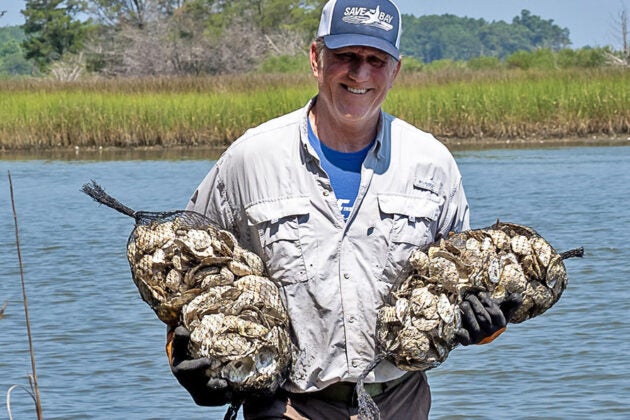 A man wearing a Save the Bay hat holds two bags of oyster shells.