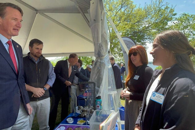 Governor Youngkin speaks with staff members at an outdoor display table featuring oyster restoration materials under a tent.
