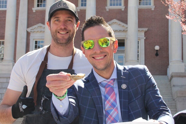 Two men pose outside the Maryland State House and one holds an oyster shell.