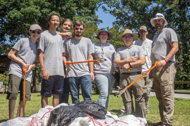 A group of volunteers with litter grabbers pose beside bags of collected trash.
