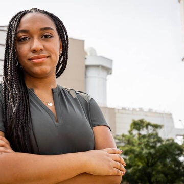 Taylor Lilley stands infront of an industrial building with a smoke stack labeled Resco.