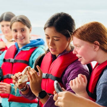 Four female students in red life jackets examine a variety of fish.