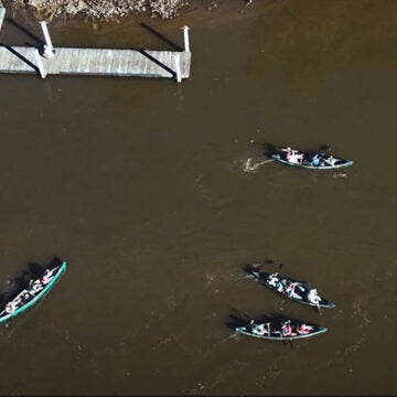 An aerial view of a dock and students paddling in several canoes.