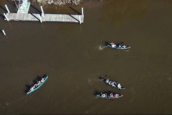 An aerial view of a dock and students paddling in several canoes.
