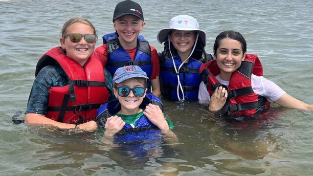 Five young girls in life jackets, grinning ear to ear as they stand in the Bay.
