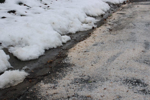 A plowed road next to a snowbank is covered in a heavy application of road salt.