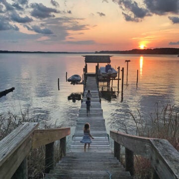 Three little girls race down a dock at sunset.