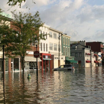 A flooded street, with water up to the top of a parked car's tires.