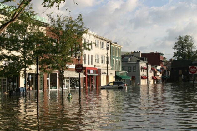 A flooded street, with water up to the top of a parked car's tires.