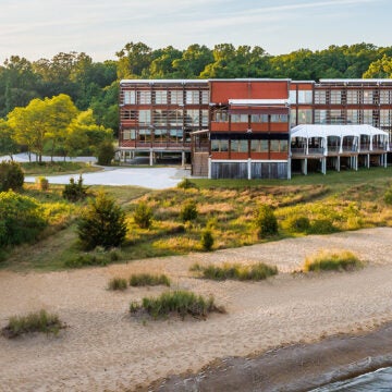 A three story building fronted with windows sits just behind a beach.
