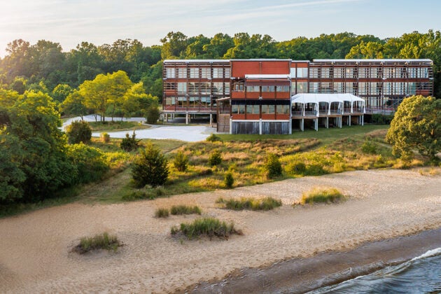 A three story building fronted with windows sits just behind a beach.